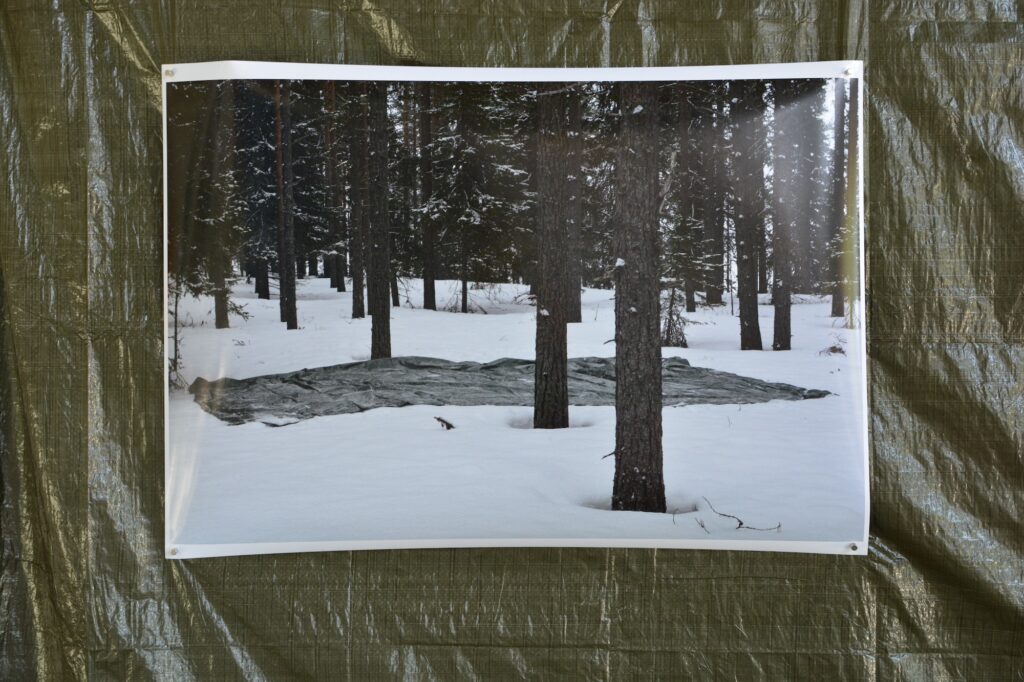 Fotografi på presenning som föreställer en grön presenning på snötäckt mark i skog. Del av installationen Dangerous Grounds på Slakthuset Göteborg.